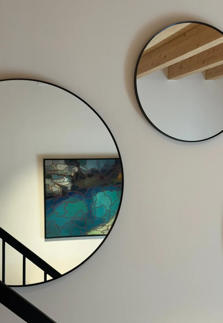 A composition of circular mirrors brings reflected views of timber and art to the light wall beside the stairs.
