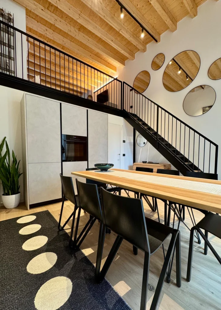 Loft in Monza A black steel staircase connects the dining space to the mezzanine, with circular mirrors softening its linear geometry.
